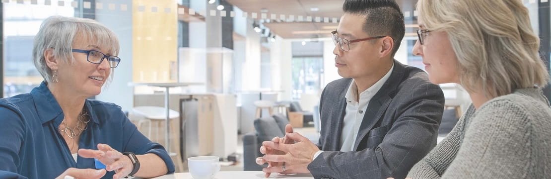 A man and woman couple sit on the right side of a table and are conversing with a woman seated on the left side of the table